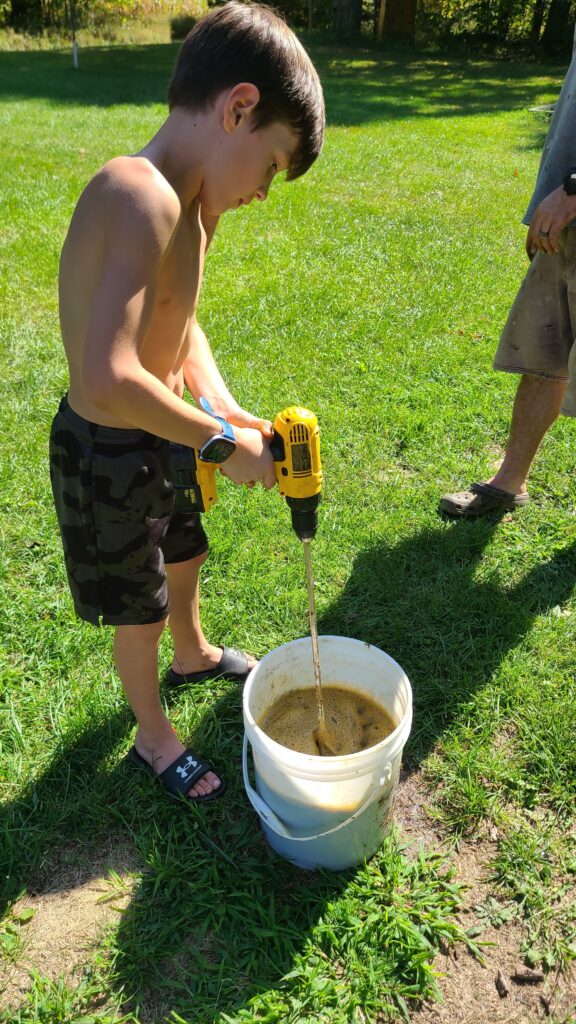 Boy using a power drill with paint attachment to mix walnuts and water
