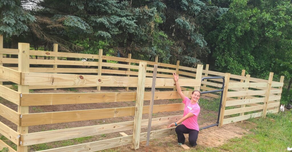 Girl in front of a wooden goat enclosure