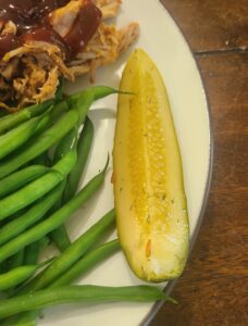 Homemade refrigerator dill pickle spear with pulled pork and green beans on a plate