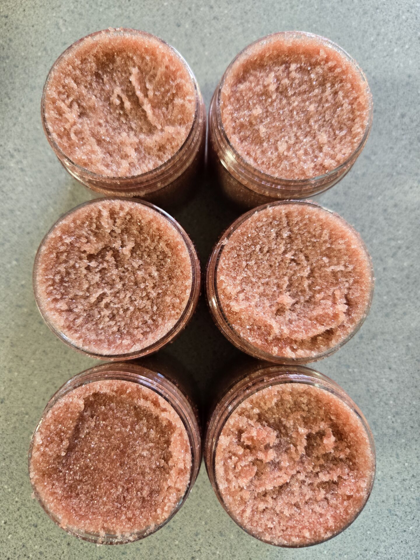 Six reddish, orange homemade sugar scrubs sitting on a countertop.