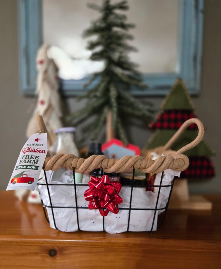 A gift basket with handmade skin care items on a table in front of 3 Christmas trees.