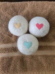 Three felted mohair dryer balls with hearts on them sitting on a towel