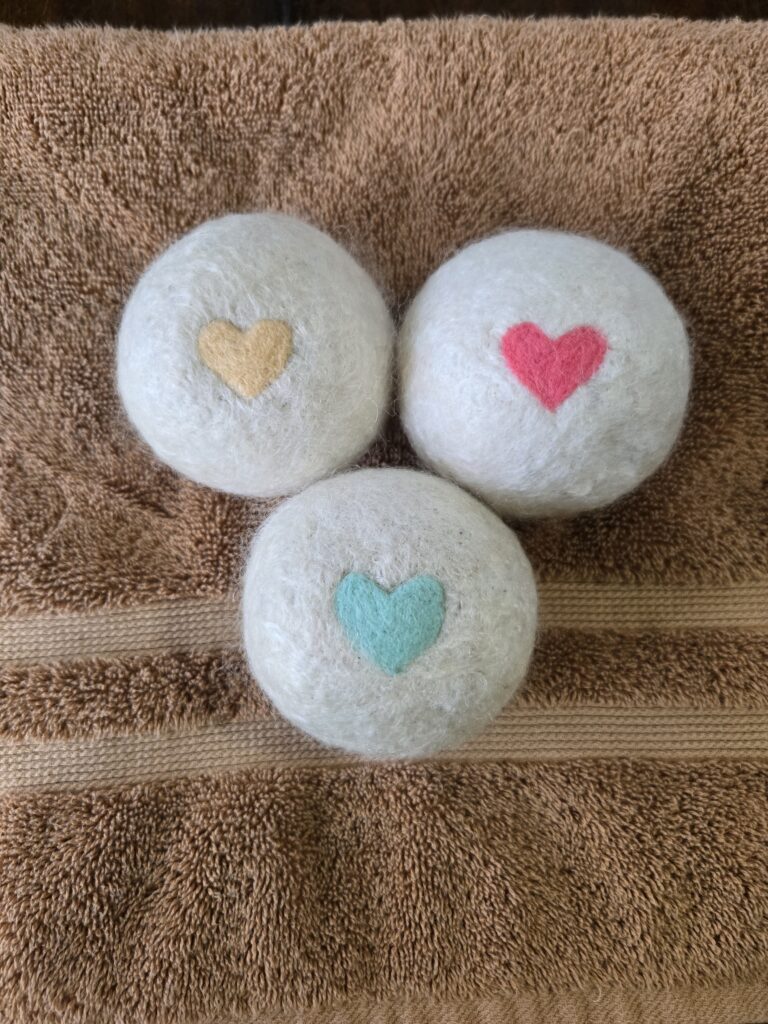 Three felted mohair dryer balls with hearts on them sitting on a towel