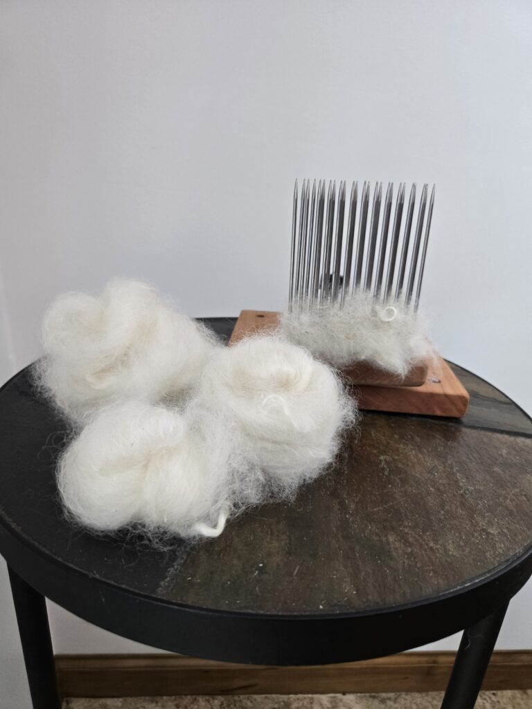 Three nests of combed top on a table in front of a wool comb and hackle.