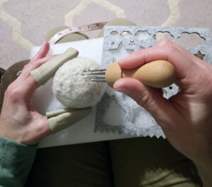 One hand with finger protection holding a dryer ball and the other hand using a multi-needle felting tool