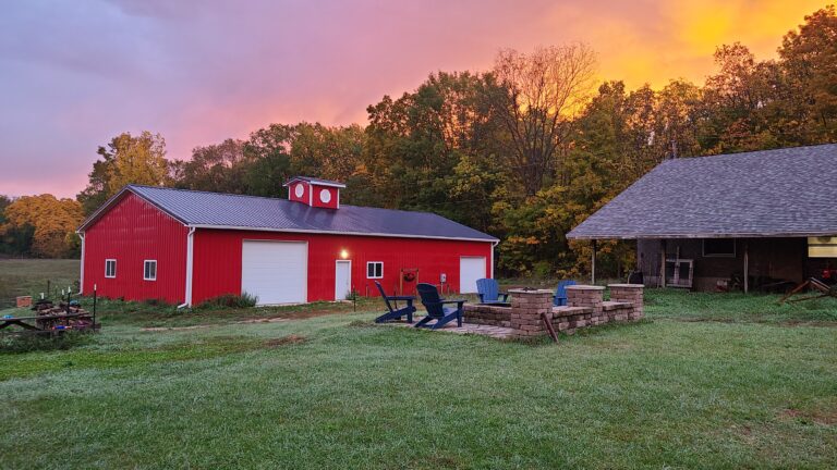 A red barn with a fire pit and a sunset in the background.