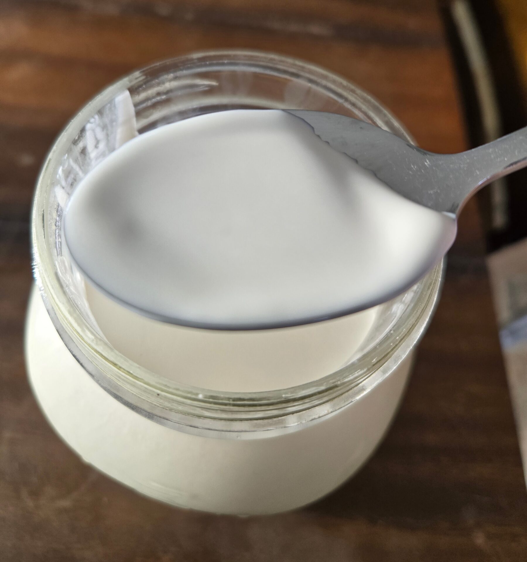 A spoon holding cream on the top of a milk jar