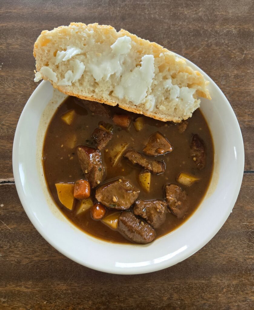Bread with goat butter sitting on a bowl of stew.