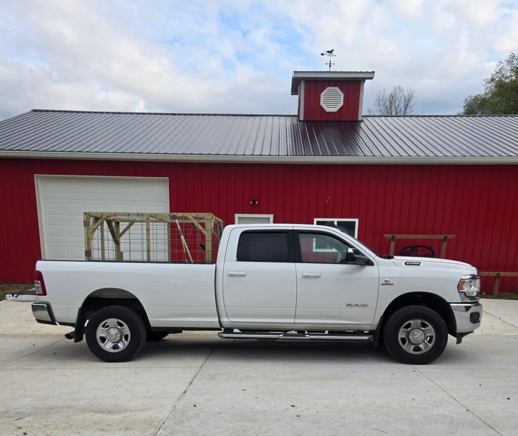 White truck with a livestock hauler in the bed parked in front of a barn.