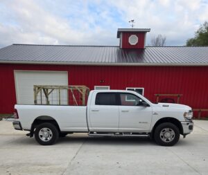White truck with a livestock hauler in the bed parked in front of a barn.