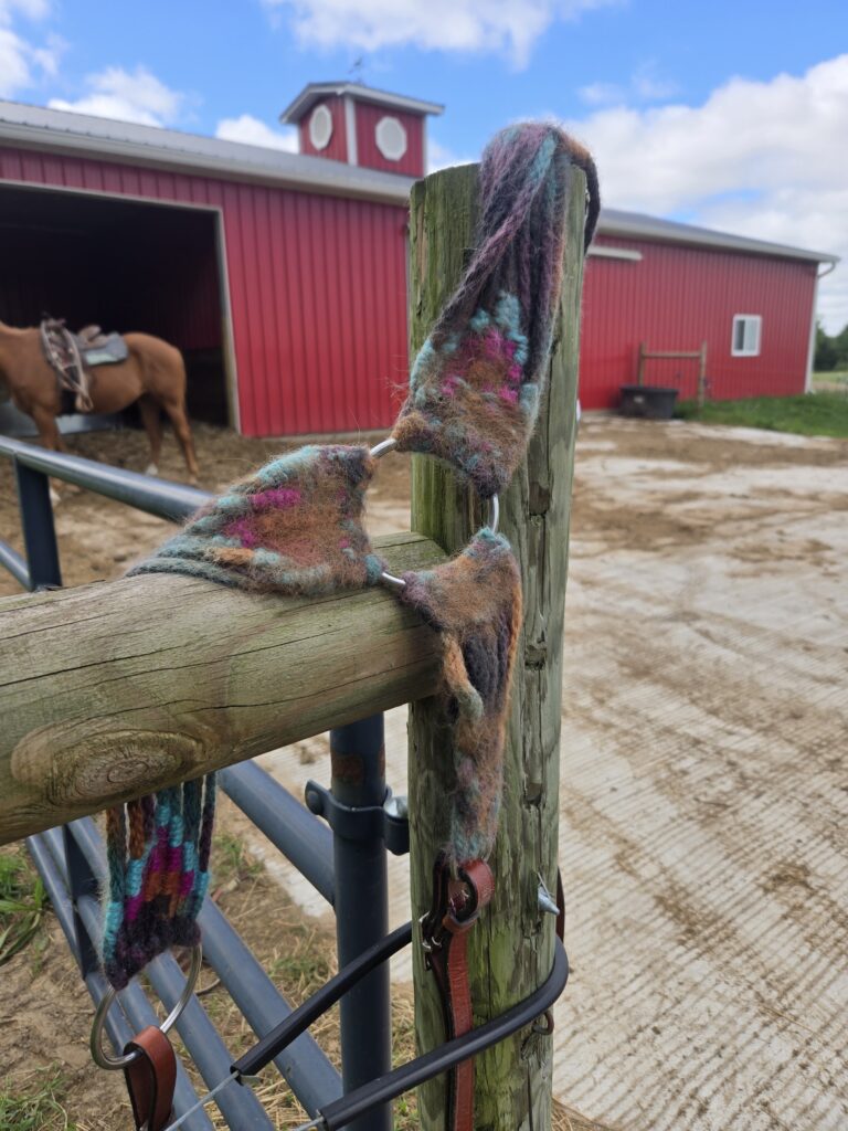 A mohair breast collar hanging on a fence in front of a red barn,