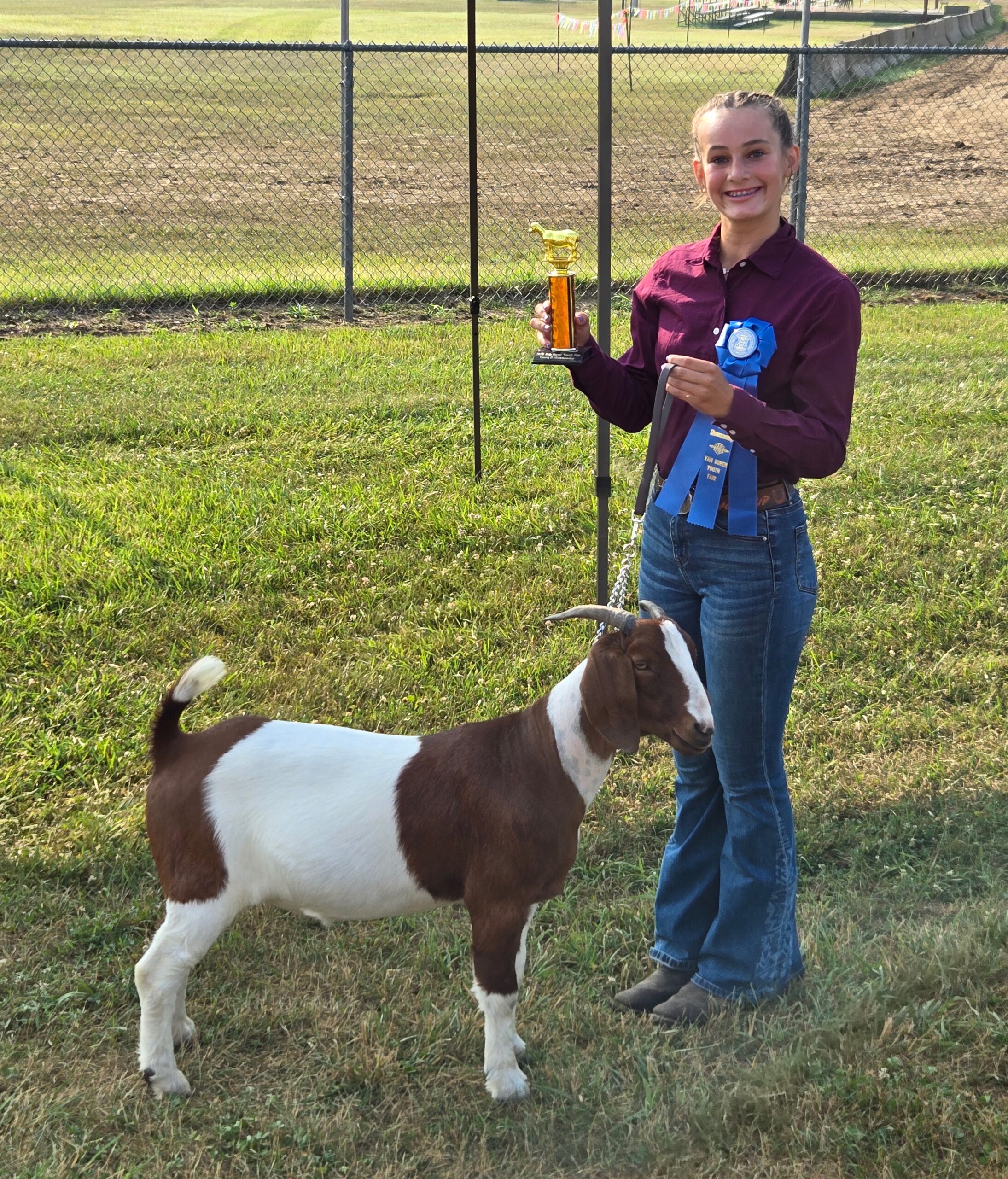 Girl with a goat holding a blue ribbon and trophy