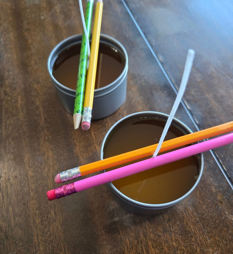 Freshly poured candles with pencils on top of them keeping the wicks straight.
