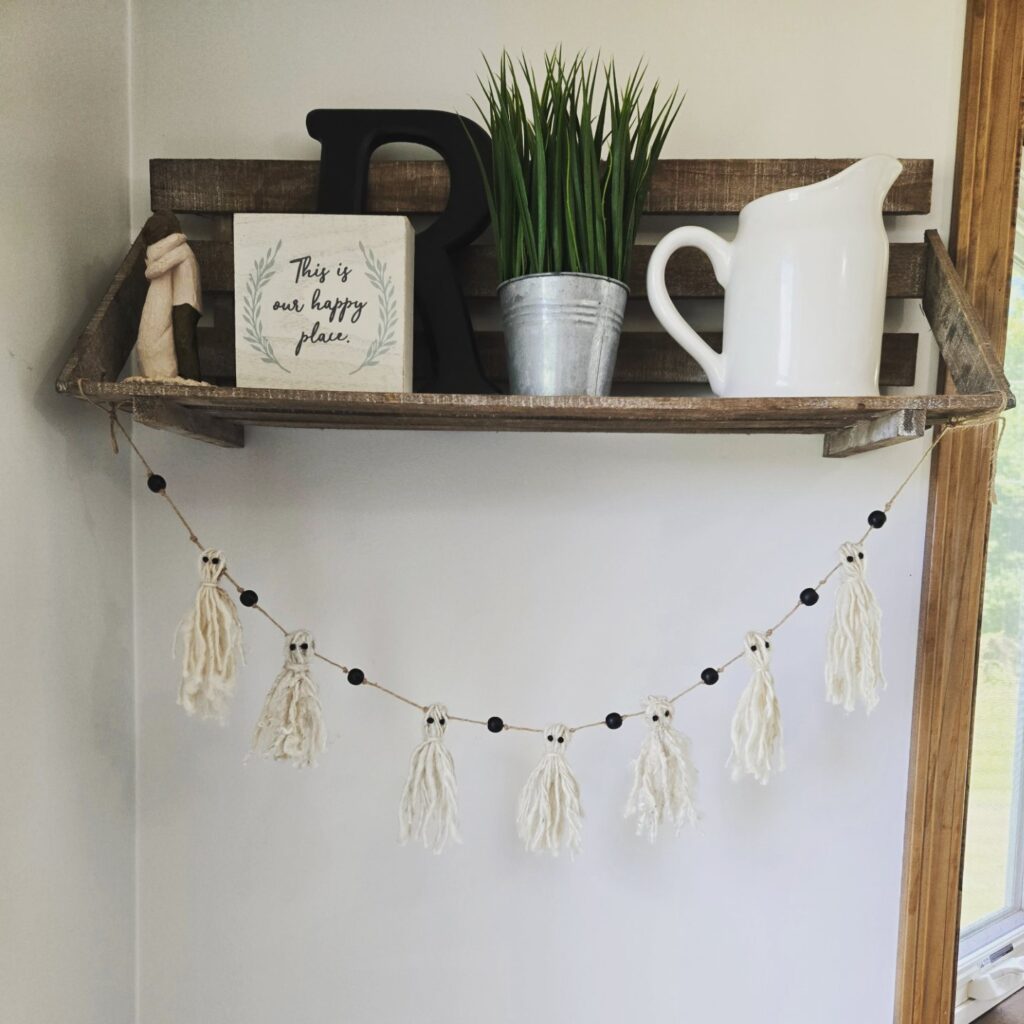 A handmade rustic yarn ghost garland hanging from a shelf