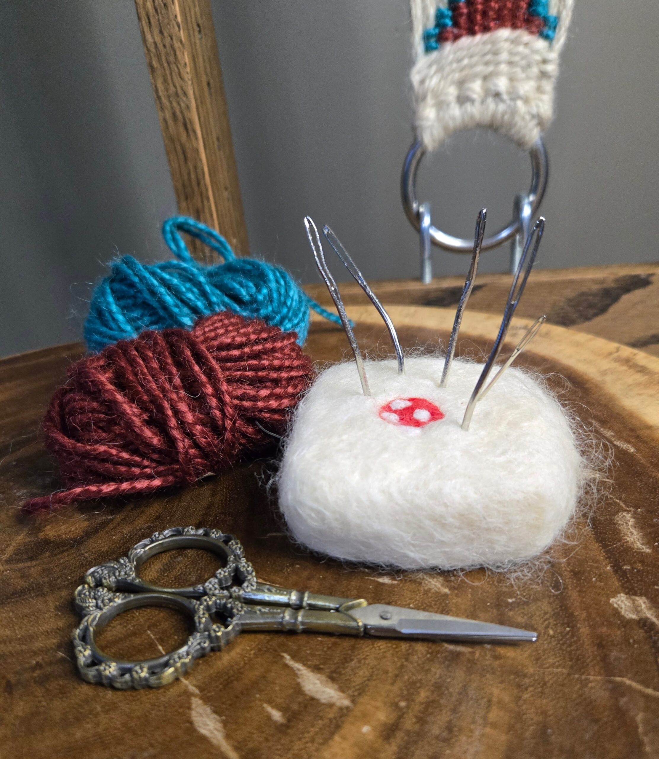 Felted soap pin cushion with a weaving project and scissors.
