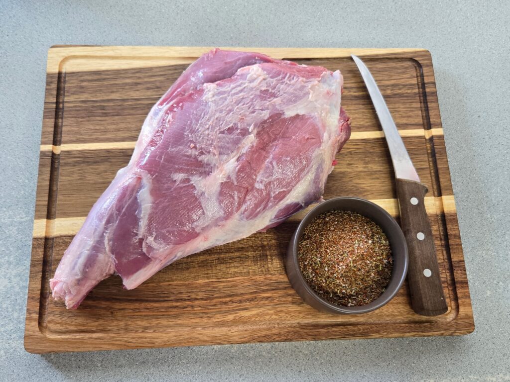 Goat leg on a cutting board with a knife and spices.