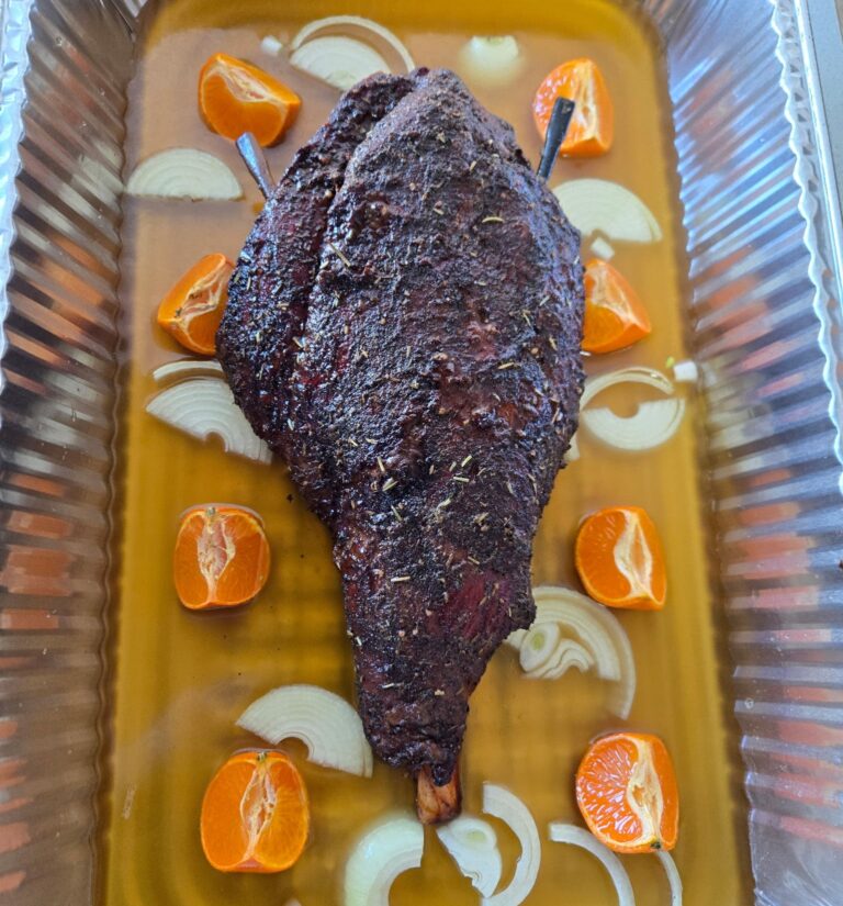 Smoked goat leg in a pan with oranges and onions.