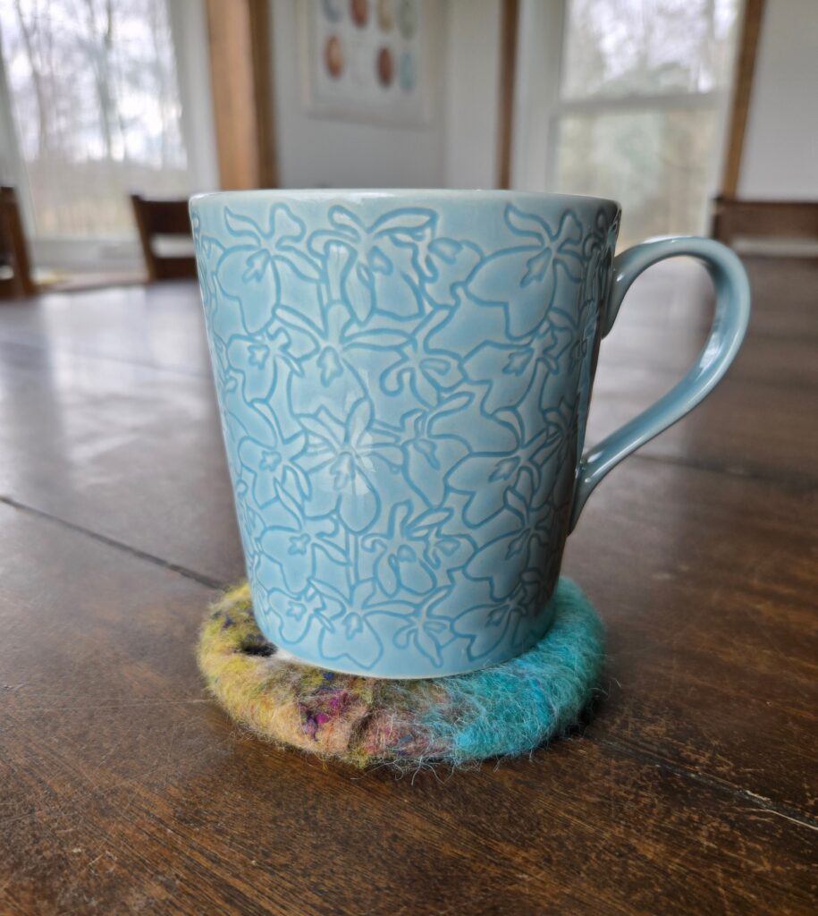 A cup of coffee resting on a wet-felted coaster.