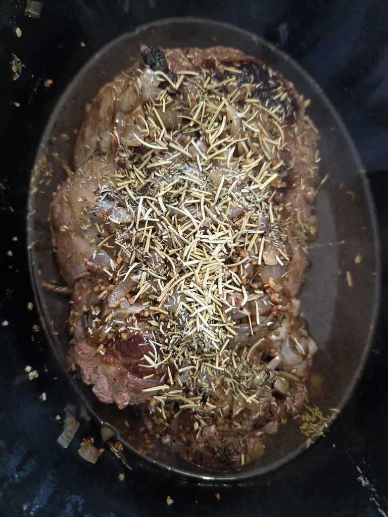 Slow cooker goat pot roast in a crock pot with herbs.